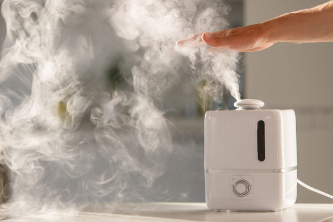 Man Holds Hand Over Steam Aroma Oil Diffuser On The Table At Hom