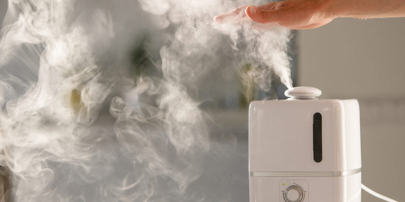 Man Holds Hand Over Steam Aroma Oil Diffuser On The Table At Hom